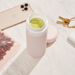 Blush wide mouth ceramic Porter waterbottle with green matcha latte inside. Phone, keys, and bag of almonds on counter. 