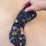 Hand holding Slow North migraine mask over wooden background. Eye pillow is navy with floral design. 