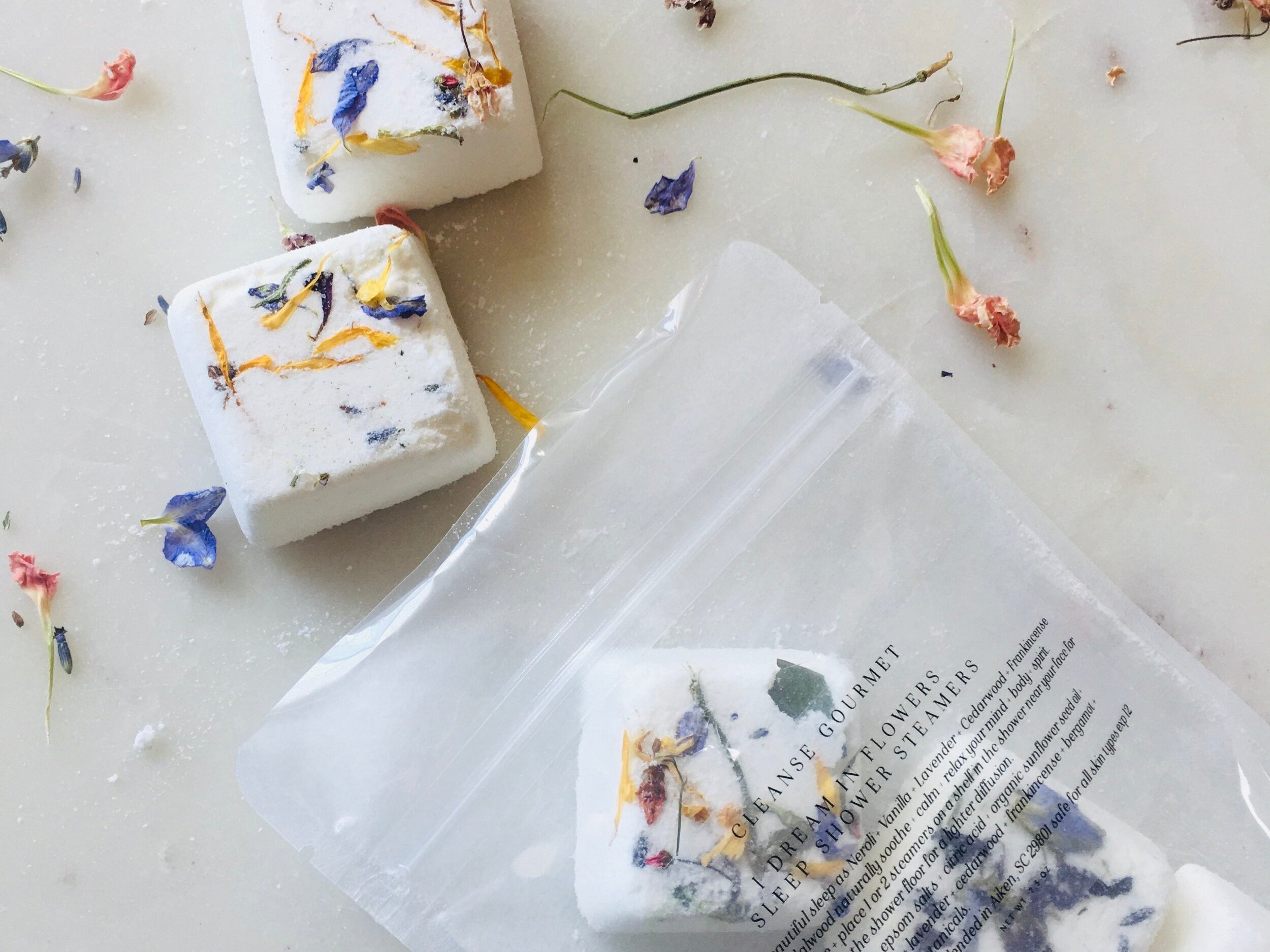 I Dream in Flowers Botanical Shower Steamers by Cleanse Gourmet with French lavender and vanilla essential oils. Five cubes in and out of packaging, surrounded by dried flowers. 