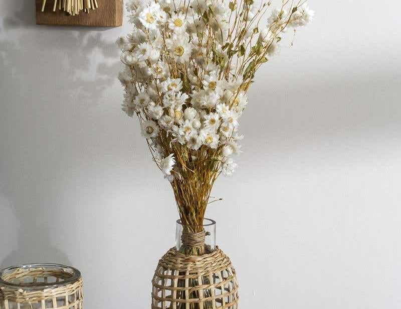 Two Jaxon Caraffes made of rattan covered glass, set in home and holding dried white flowers.