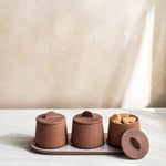 Canyon Decorative Spice Jars by Citrine Set of 3. Crafted from exposed reddish-brown earthenware with white glaze. Paired with tray and one lid off and holding sugar cubes.