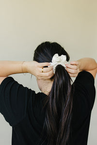 The Ivory crystal mulberry silk scrunchie, set with tiny rhinestones, tied around a long dark ponytail seen from behind.