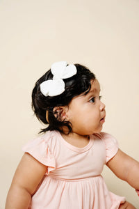 Lou Lou & Company Adventure Bow in white worn by a baby girl with dark curls in a pink top