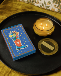 Cobalt blue Paddywax matchbox with a cowboy boot holding flowers and gold stars