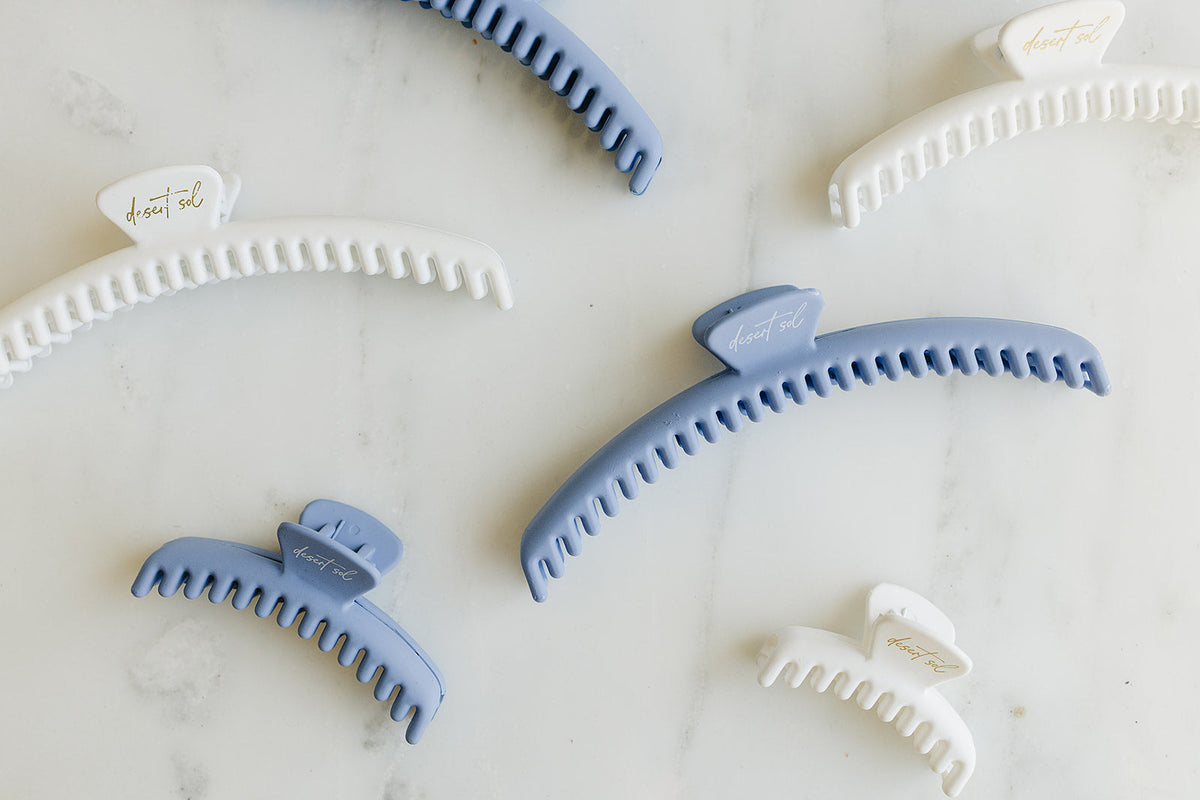 Frenchie claw clips in periwinkle blue and white in several sizes laid out on white marble, each with the desert sol script on the top tab