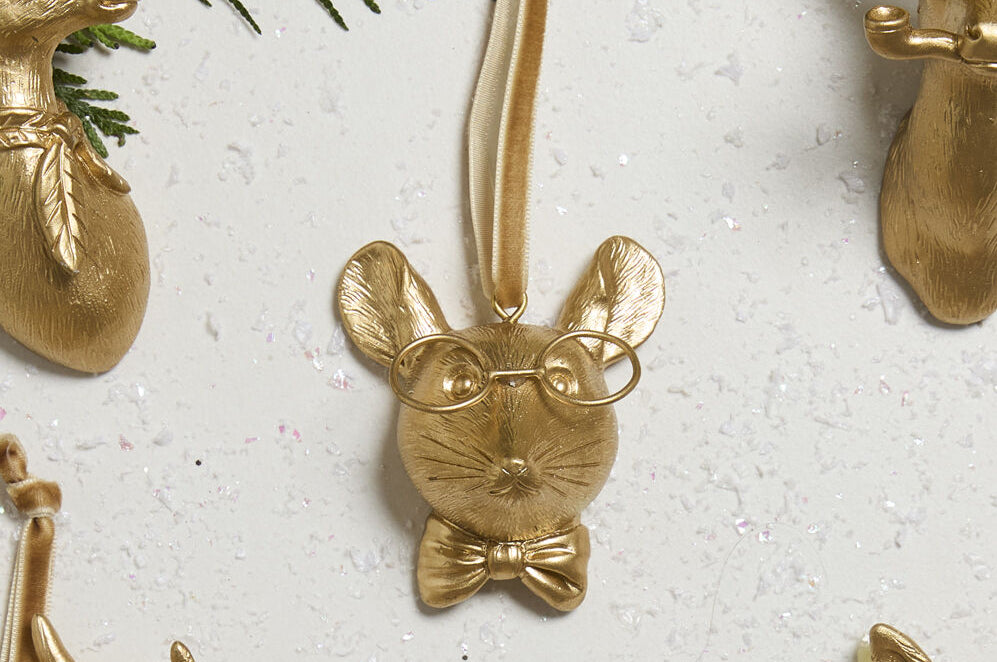 E + E Ornaments, sixteenth view, the gold mouse with a bow tie beside cedar greenery