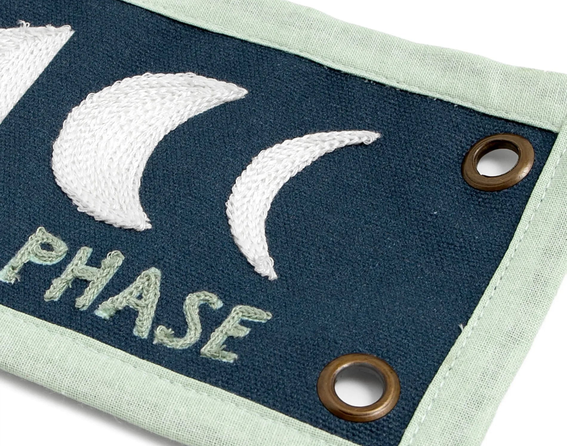 Close-up of the embroidered moon phases and brass grommet on the 1canoe2 Find Beauty Banner