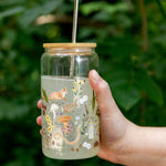 Hand holding the 1canoe2 Flora & Fauna Glass Can with a fox and wildflower print, outdoors