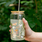 Hand holding the 1canoe2 Flora & Fauna Glass Can with a fox and wildflower print, outdoors