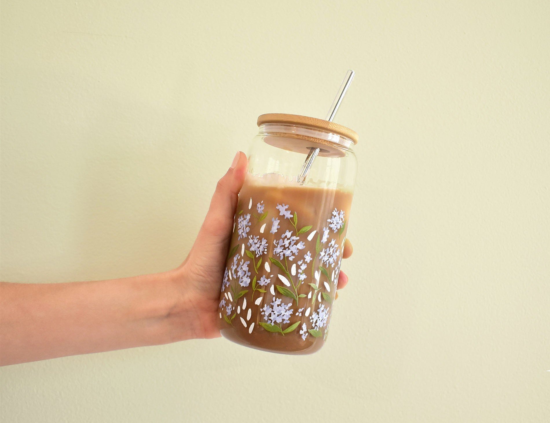 Hand holding the 1canoe2 Hydrangea Coffee Cup with a bamboo lid and straw