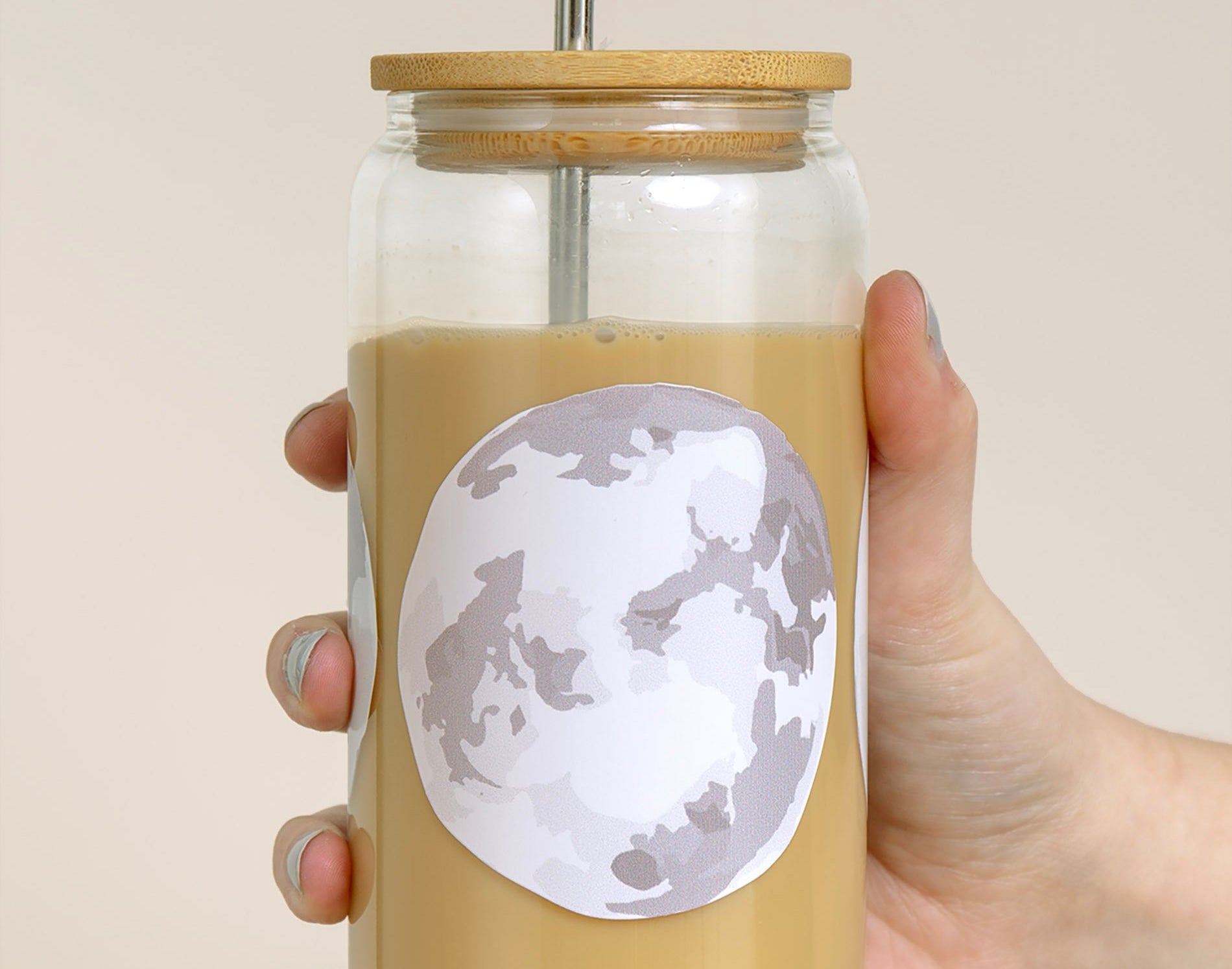 Hand holding the 1canoe2 Moon Phases Glass Can filled with an iced latte