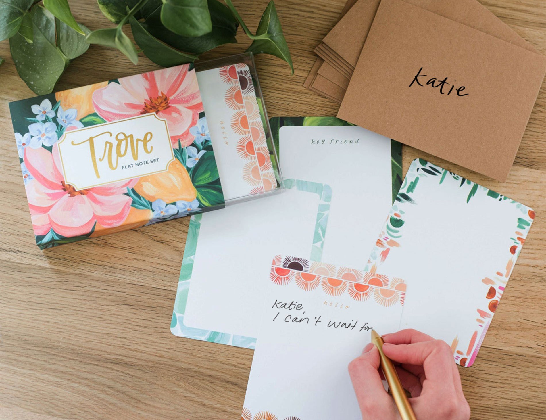 Hands writing on a 1canoe2 Trove Flat Note with kraft envelopes and the floral box
