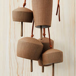 Red brown stoneware Canyon Clay Bells with leather hangings for indoor and outdoor. Five bells hanging in front of wooden background.