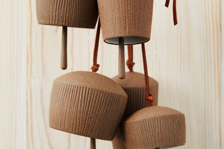 Red brown stoneware Canyon Clay Bells with leather hangings for indoor and outdoor. Five bells hanging in front of wooden background.