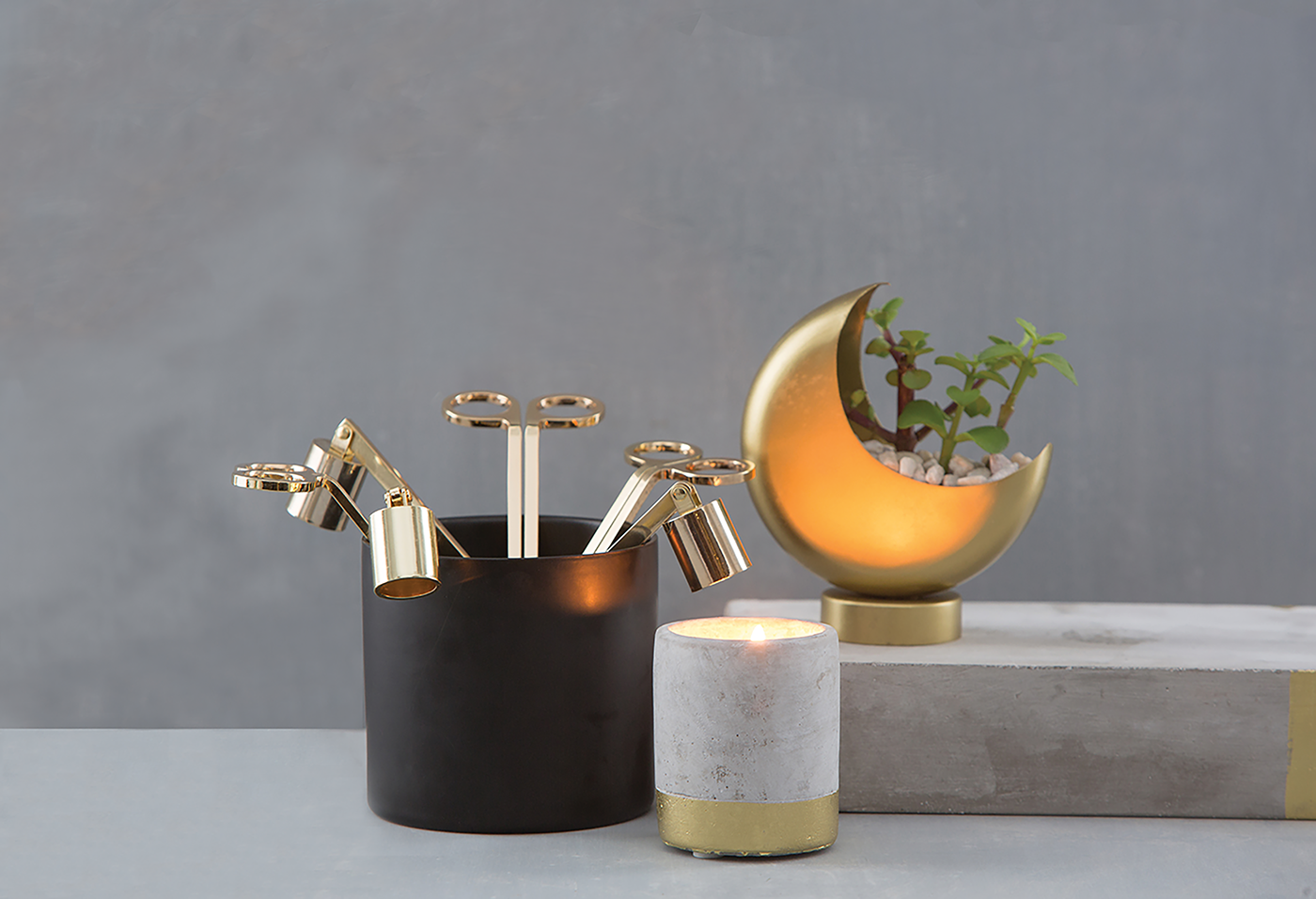 Brown vase holding three Golden Candle Snuffers by Designworks and set on desk by candle and moon planter.