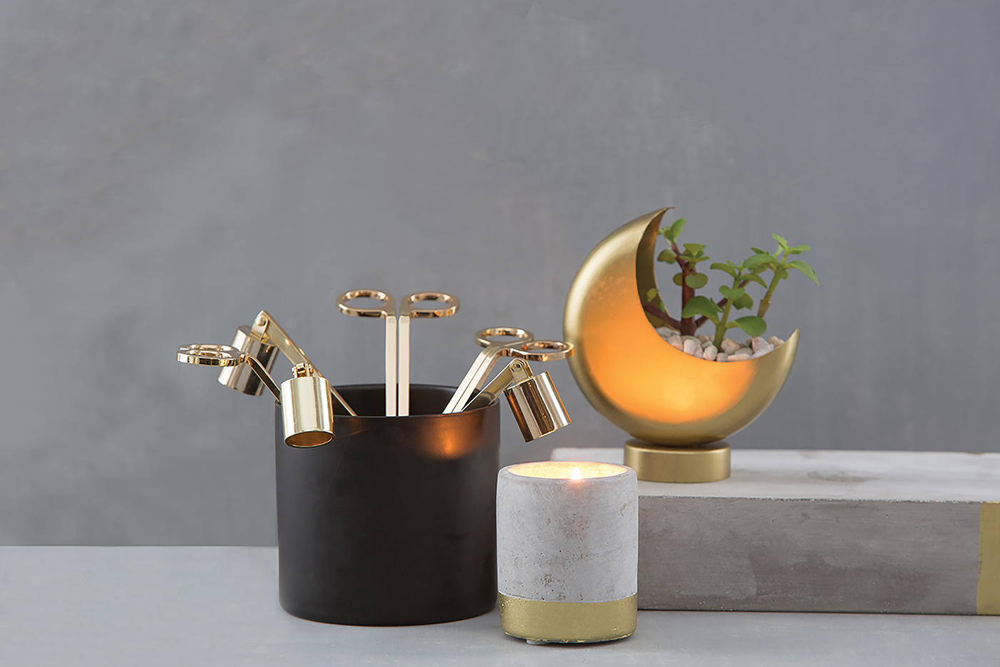 Brown vase holding three Golden Candle Snuffers by Designworks and set on desk by candle and moon planter.