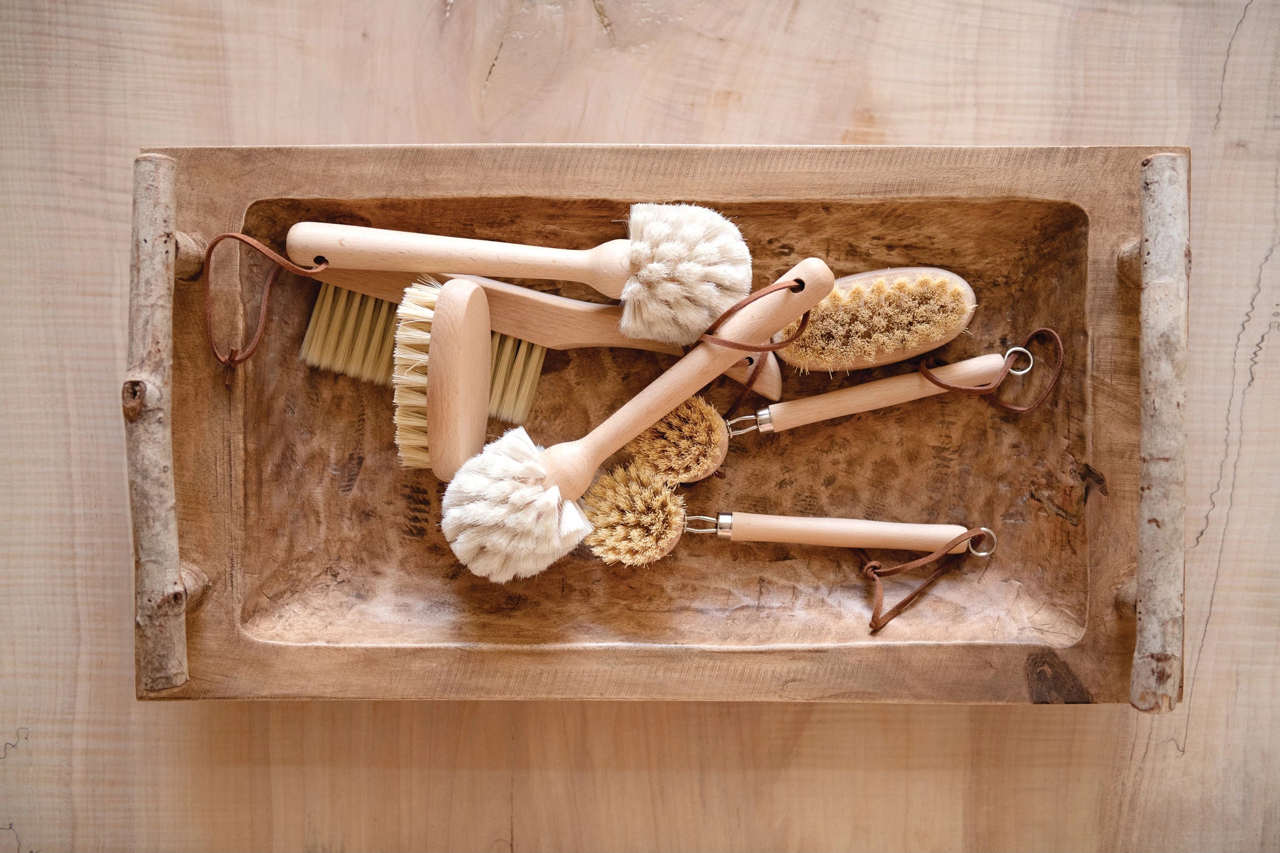 White bristle Beech Wood Dish Brush with Leather Strap and other cleaning brushes by Creative Co-Op in wooden tray.