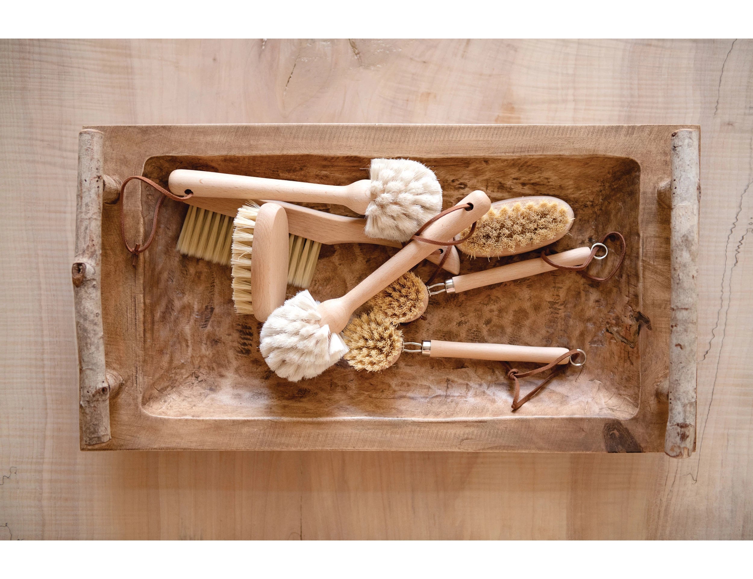 White bristle Beech Wood Dish Brush with Leather Strap and other cleaning brushes by Creative Co-Op in wooden tray.