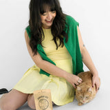 Woman in a yellow dress with a green cardigan sitting next to a cat and a bag of cat food on a white background