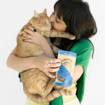 Woman holding a cat and a can of food against a white background