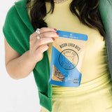 Person holding a package of 'Winnie the Winnie' bison liver bits against a white background