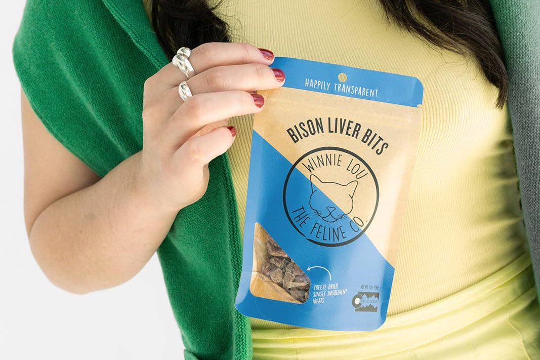 Person holding a package of 'Winnie the Winnie' bison liver bits against a white background