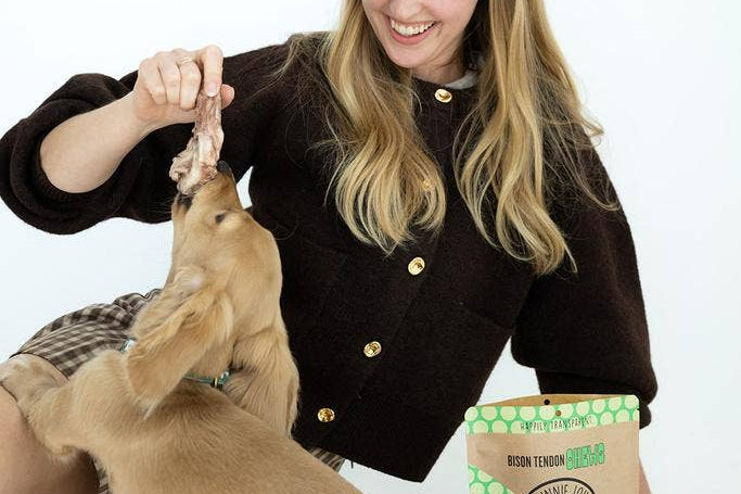 Woman playing with a dog next to a bag of dog treats on a white background
