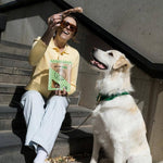 Woman sitting on steps with a dog, both looking up, in an urban setting.