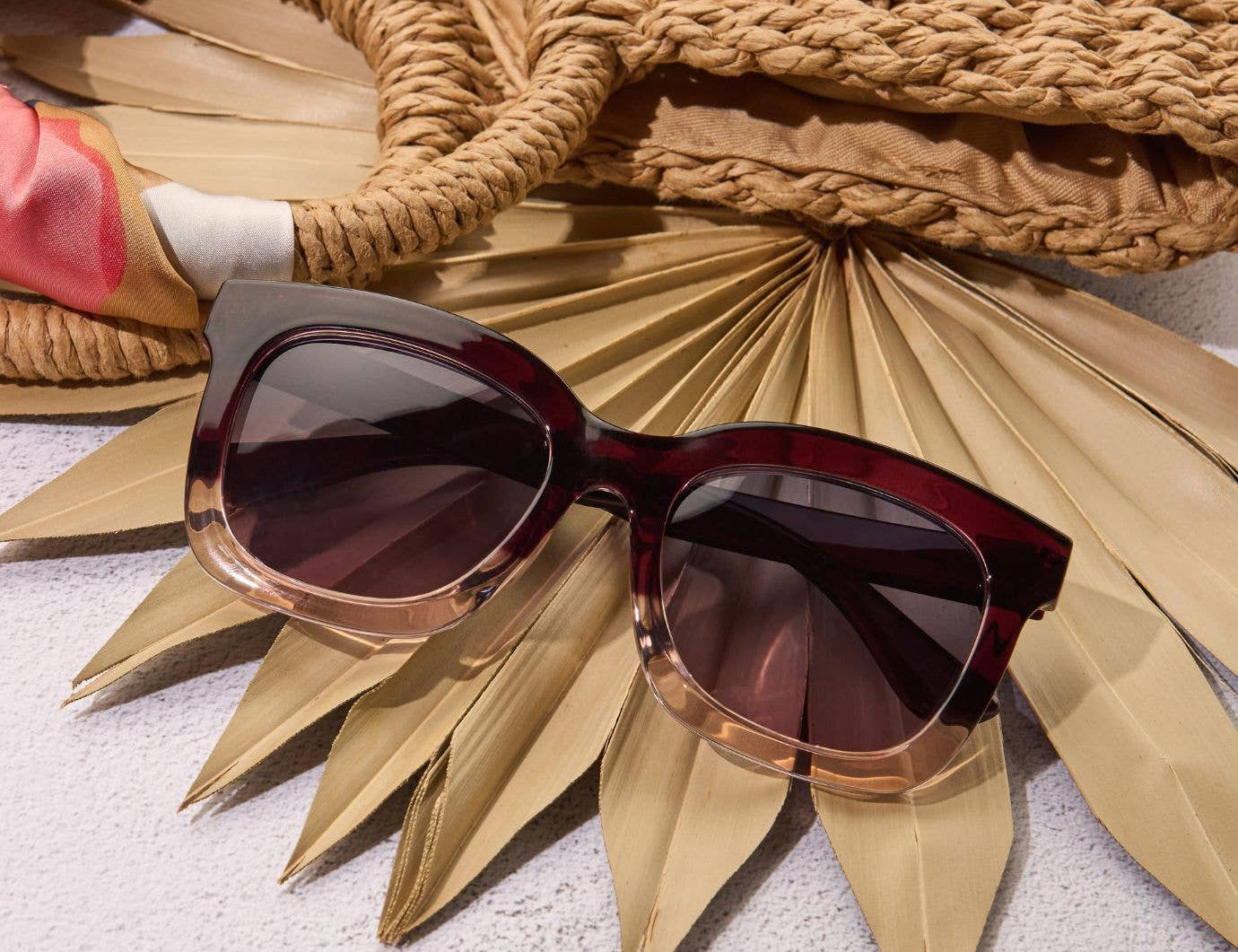 Sunglasses with a gold frame on a textured surface with a woven basket and palm leaves.