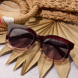 Sunglasses with a gold frame on a textured surface with a woven basket and palm leaves.