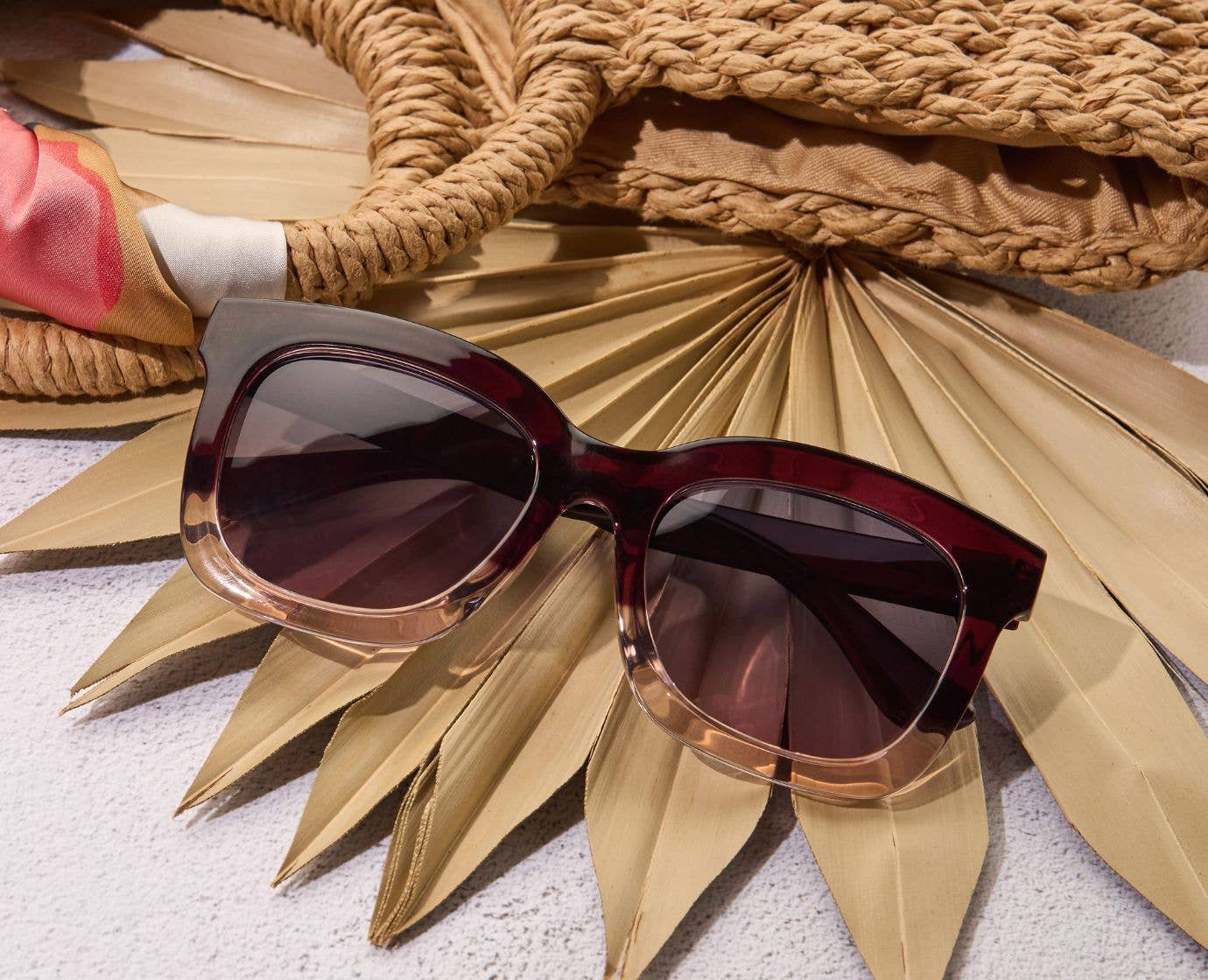 Sunglasses with a gold frame on a textured surface with a woven basket and palm leaves.