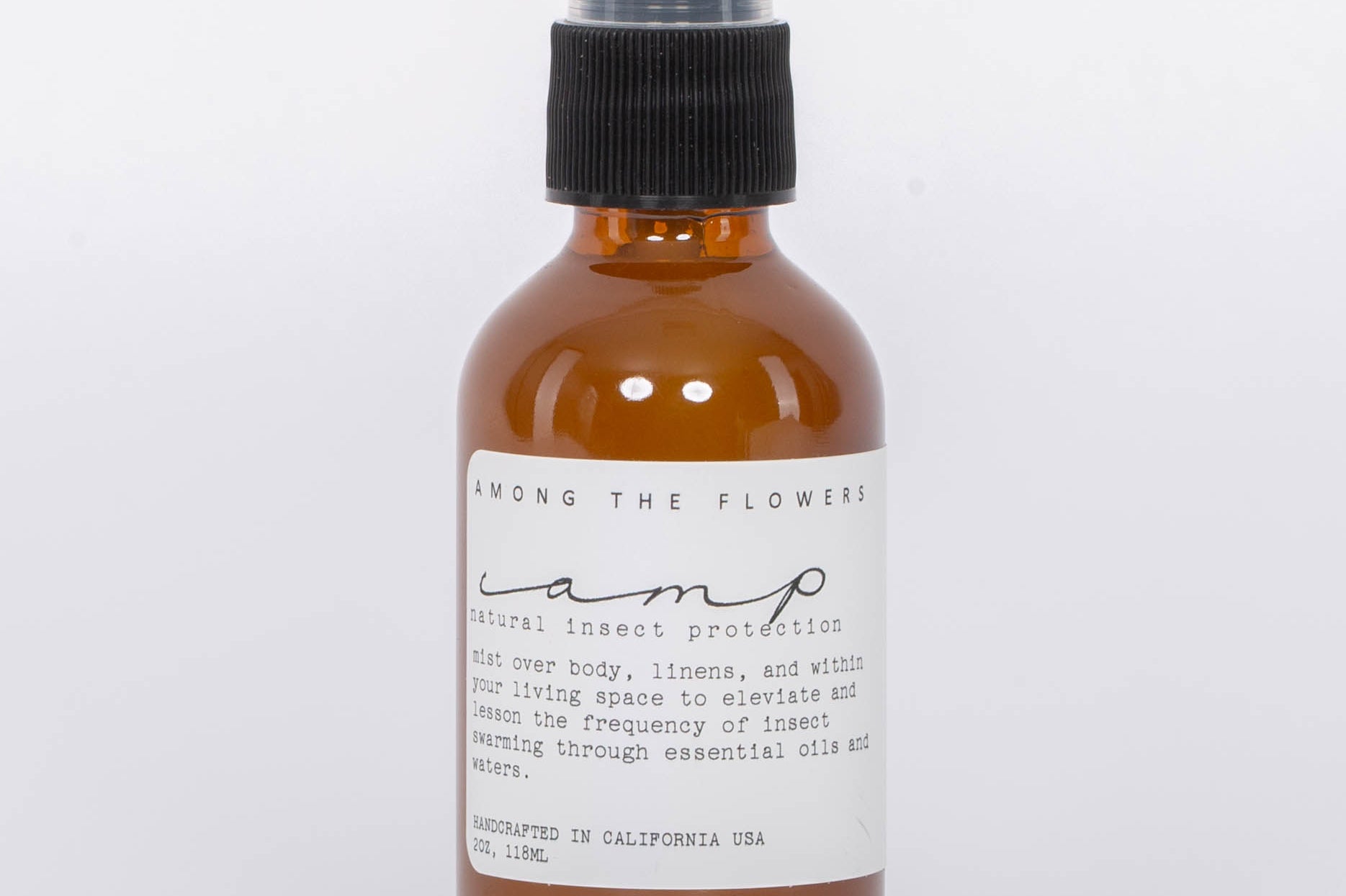 Essential oil and non-toxic Camp Mist Insect Shield by Among the Flowers in amber spray bottle with black lid and white label. White background.