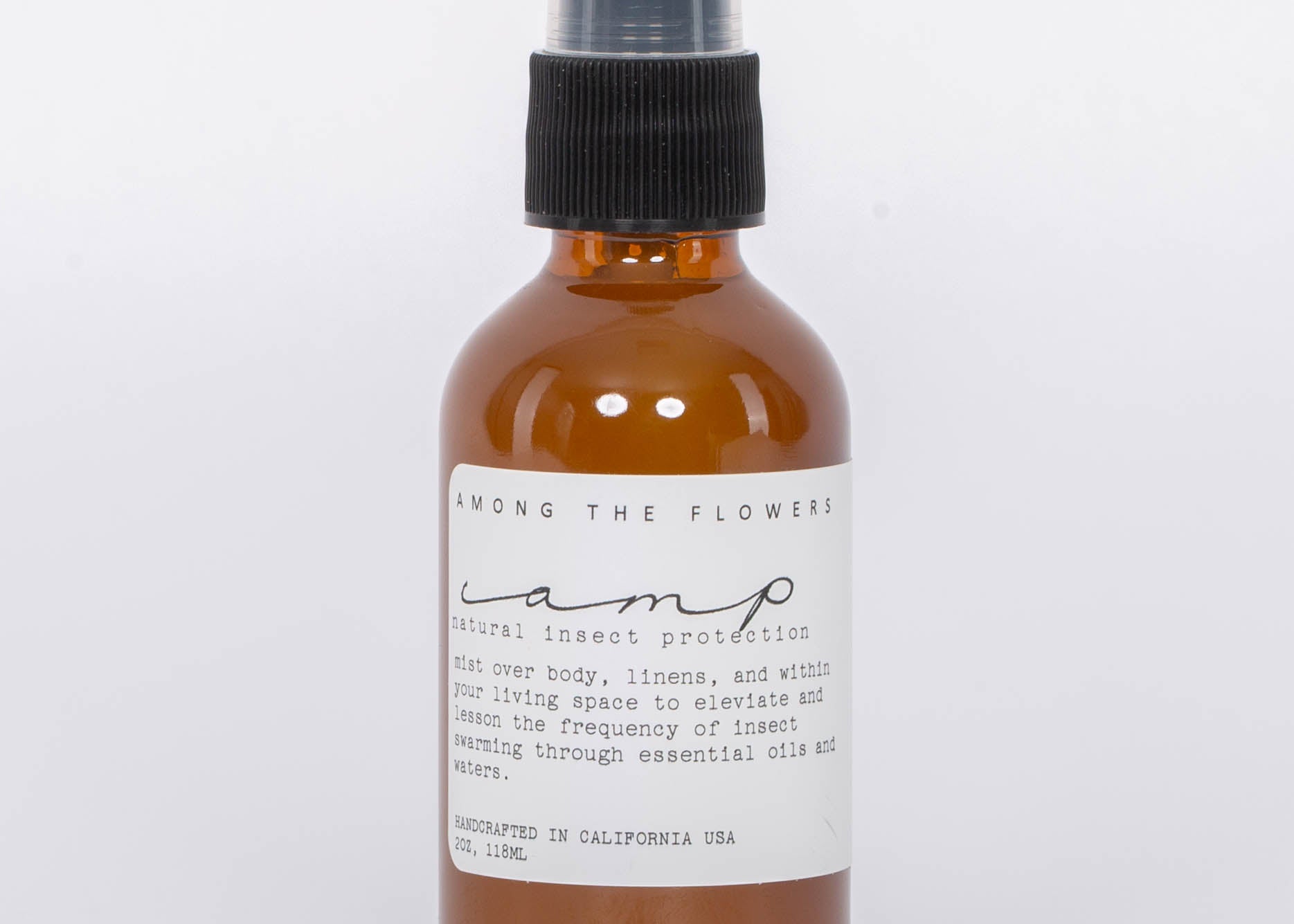 Essential oil and non-toxic Camp Mist Insect Shield by Among the Flowers in amber spray bottle with black lid and white label. White background.