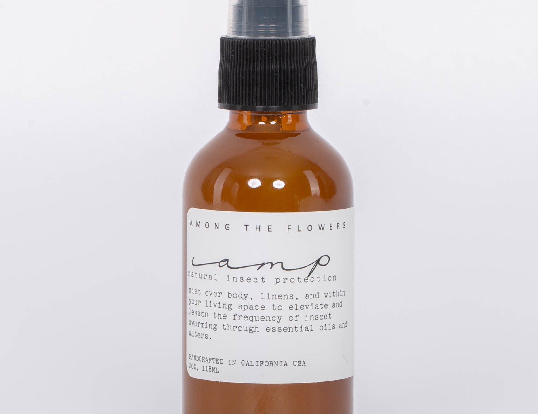 Essential oil and non-toxic Camp Mist Insect Shield by Among the Flowers in amber spray bottle with black lid and white label. White background.