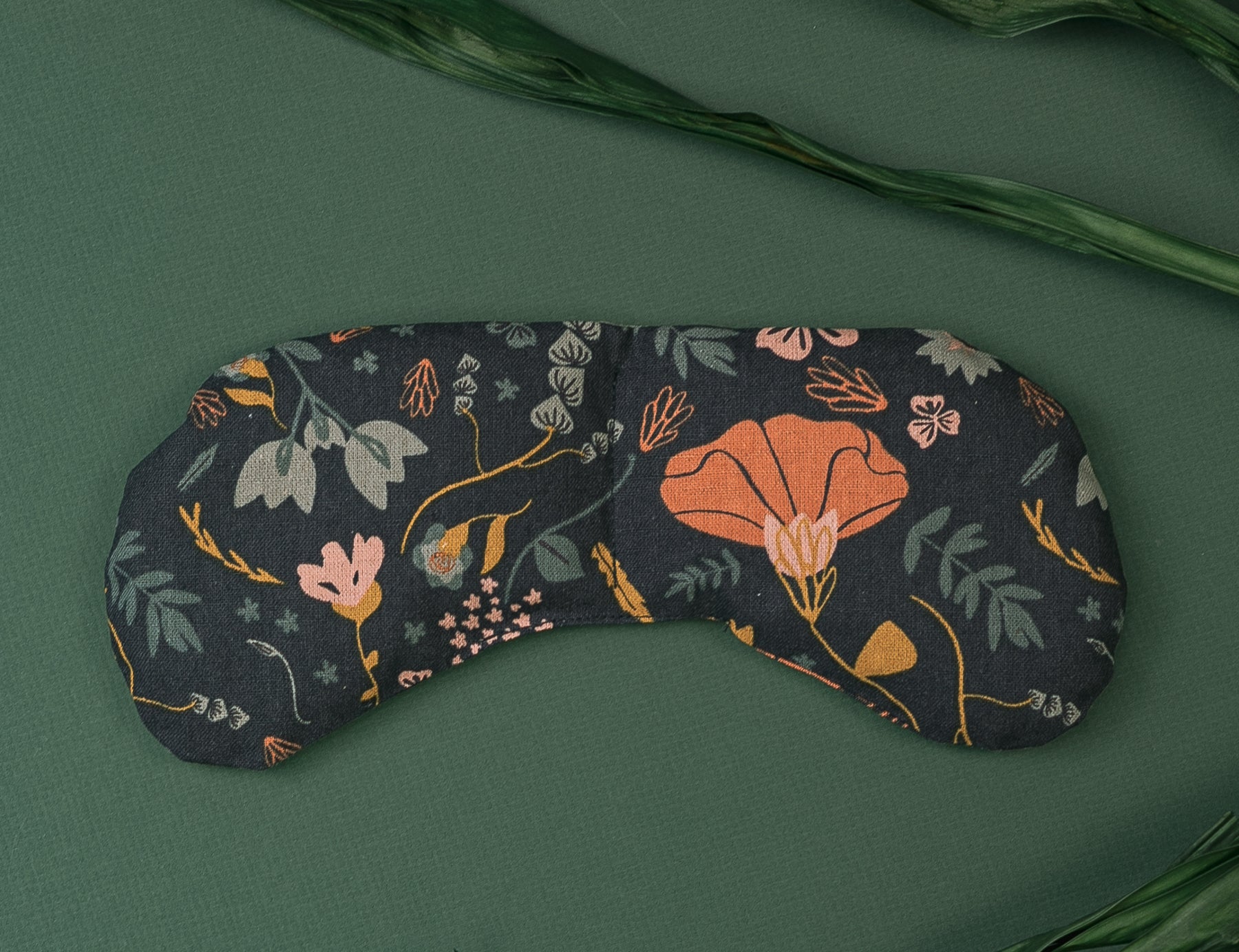 Migraine Mask by Slow North. Strap free cotton weighted eye pillow to be used hot or cold to sooth headaches and tired eyes. Navy with multicolor floral design. Dark green leaves on dark green background.