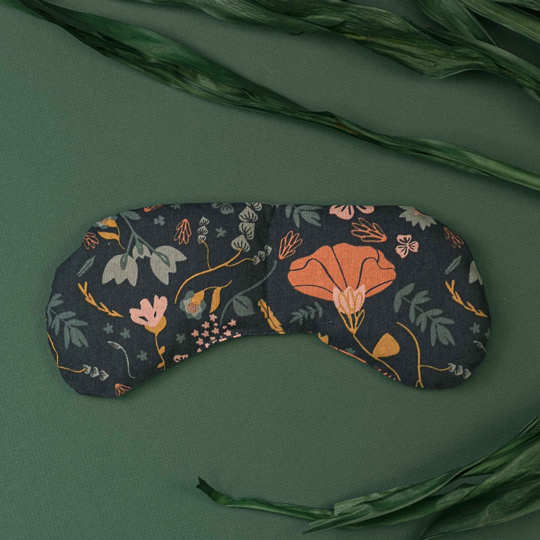 Migraine Mask by Slow North. Strap free cotton weighted eye pillow to be used hot or cold to sooth headaches and tired eyes. Navy with multicolor floral design. Dark green leaves on dark green background.