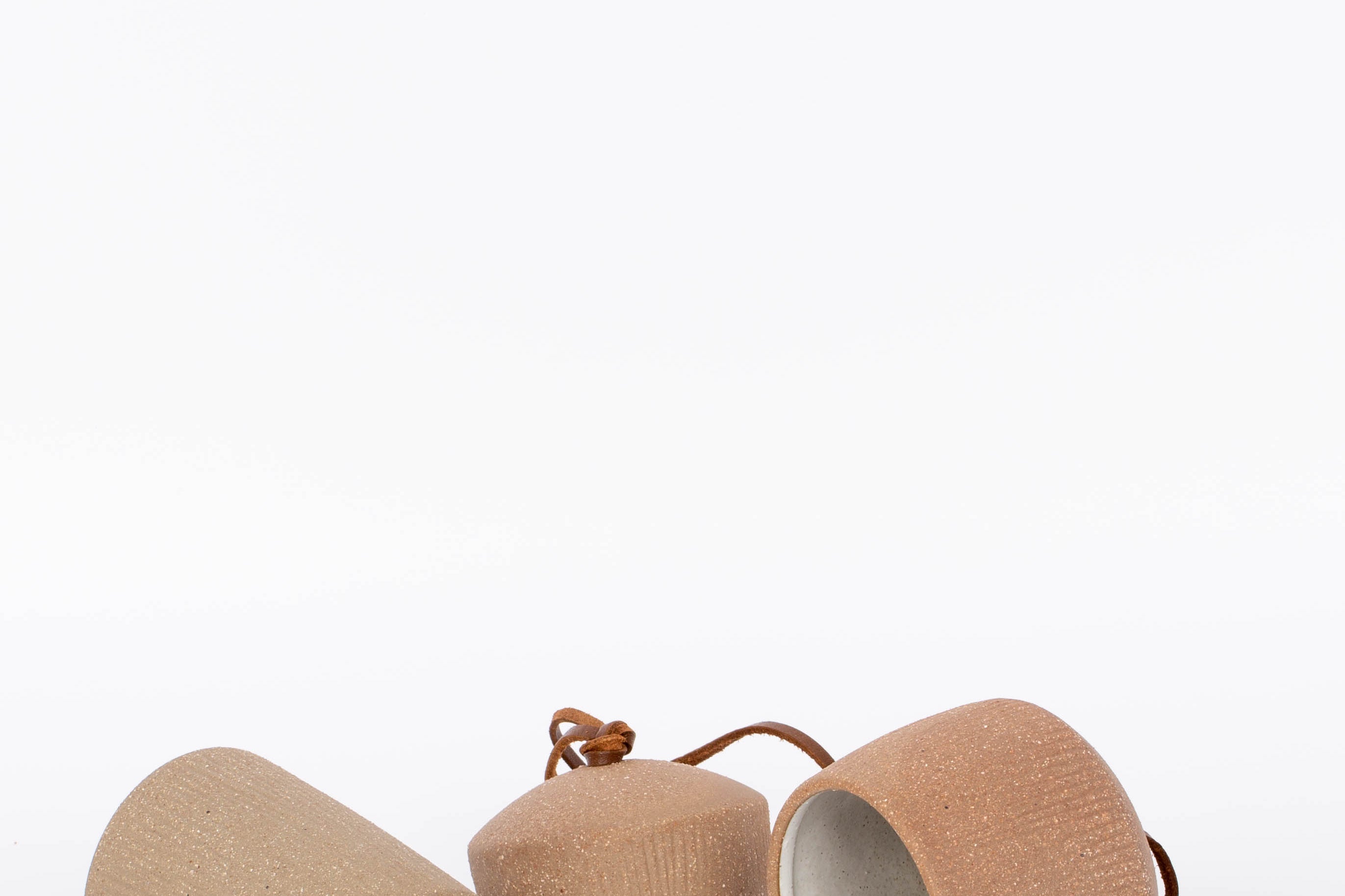 Red brown stoneware Canyon Clay Bells with leather hangings. Set of 3 sizes for indoor and outdoor. White background.