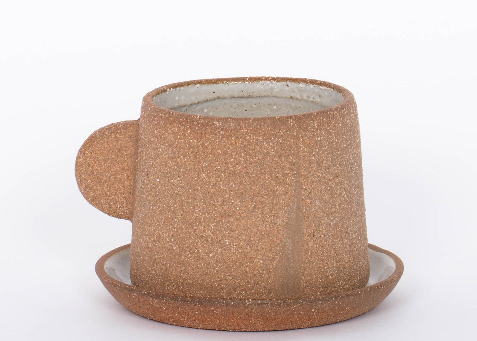 Canyon Clay Cup and Saucer with small handle by Citrine made from exposed reddish-brown earthenware and finished with a thin off-white glaze. 