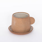 Canyon Clay Cup and Saucer with small handle by Citrine made from exposed reddish-brown earthenware and finished with a thin off-white glaze. 