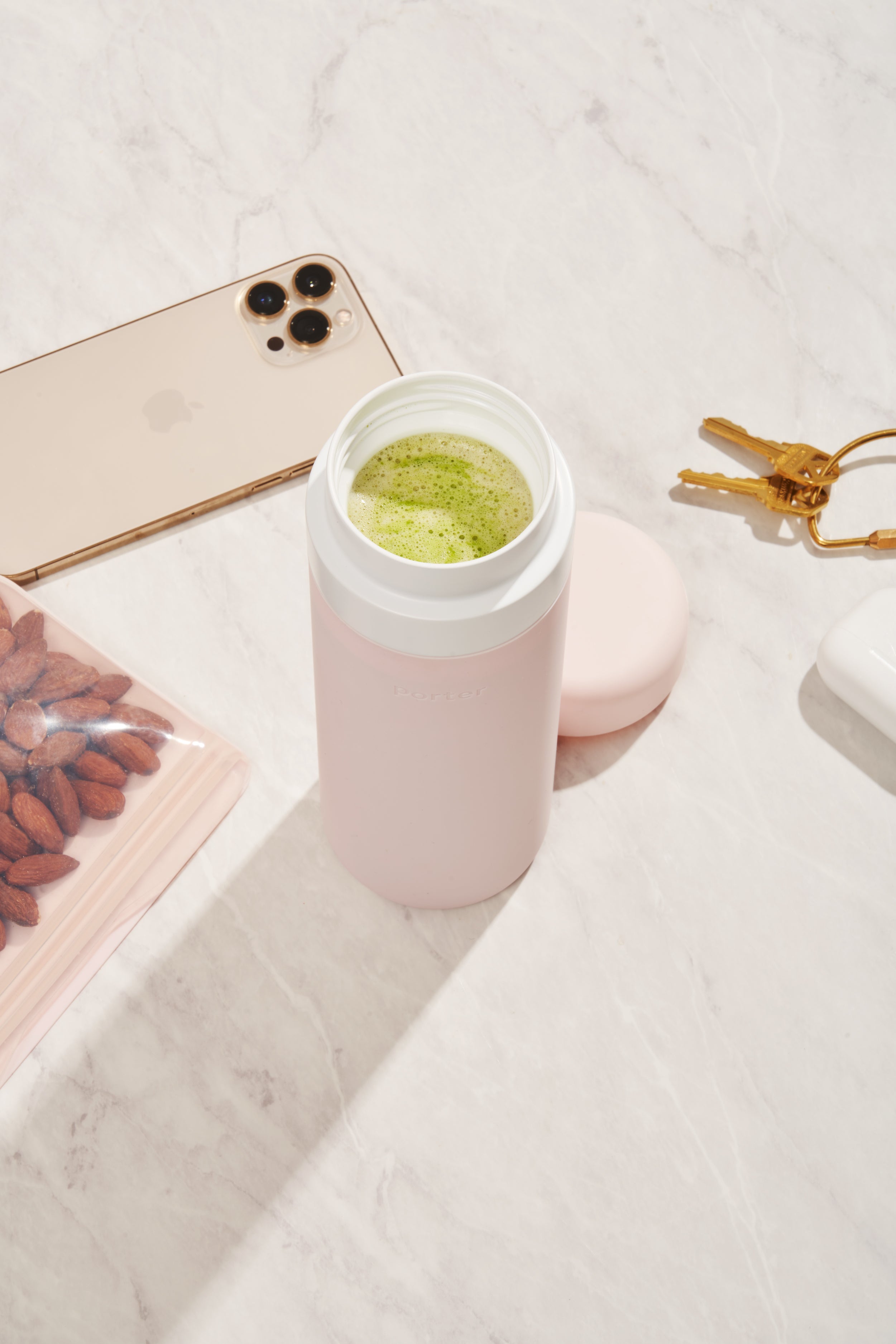 Blush wide mouth ceramic Porter waterbottle with green matcha latte inside. Phone, keys, and bag of almonds on counter. 