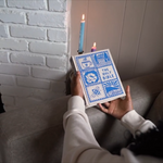 Person holding a book titled 'The Holy Bible' with blue cover design, sitting on a couch.