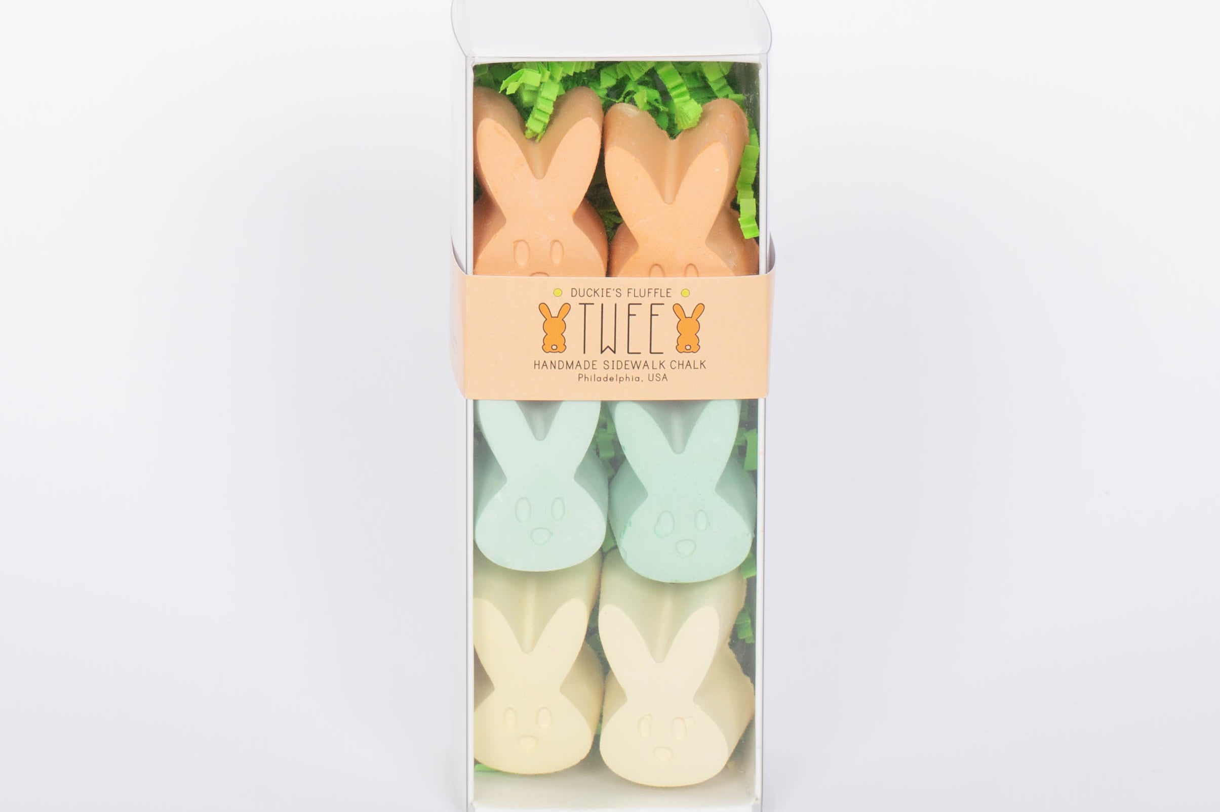 Box of TWEE six piece children's bunny shaped chalk in orange, yellow, and green. White background.