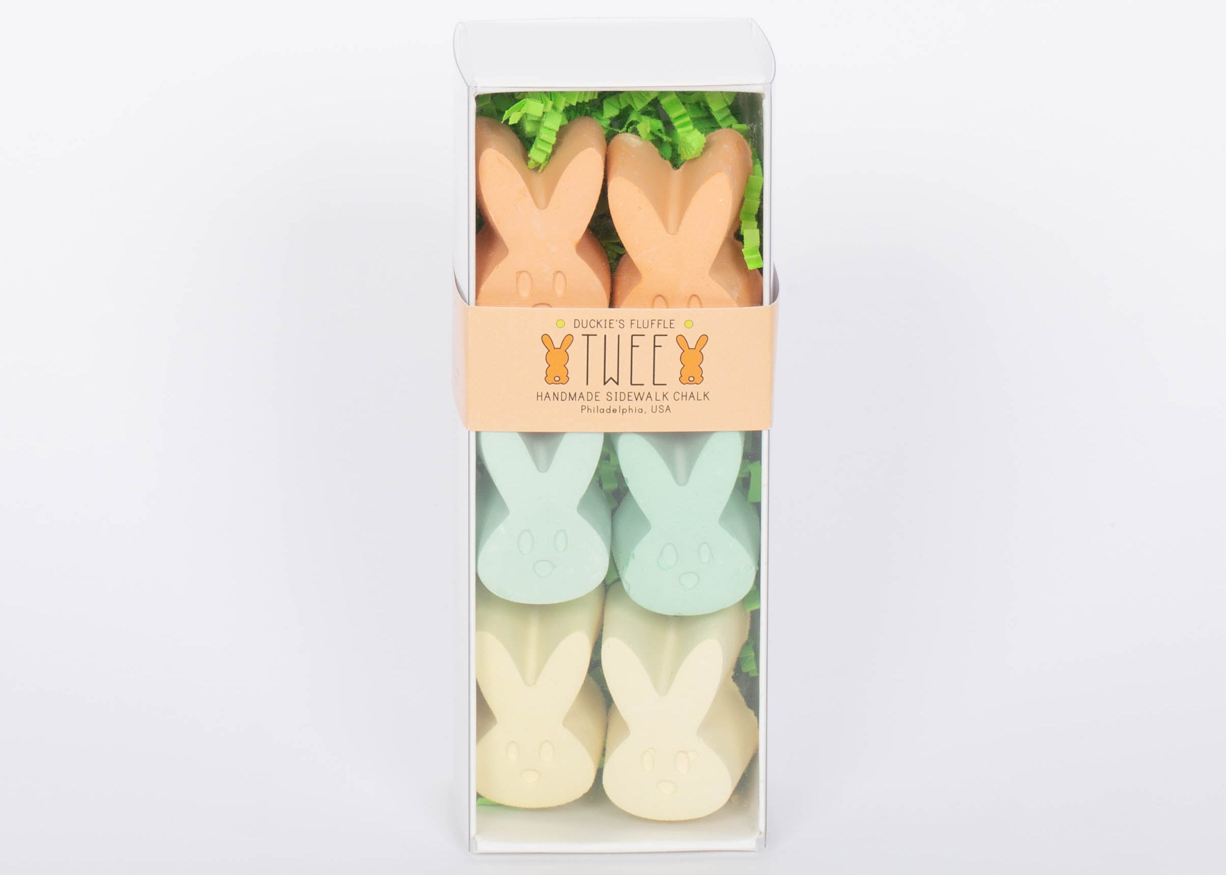 Box of TWEE six piece children's bunny shaped chalk in orange, yellow, and green. White background.