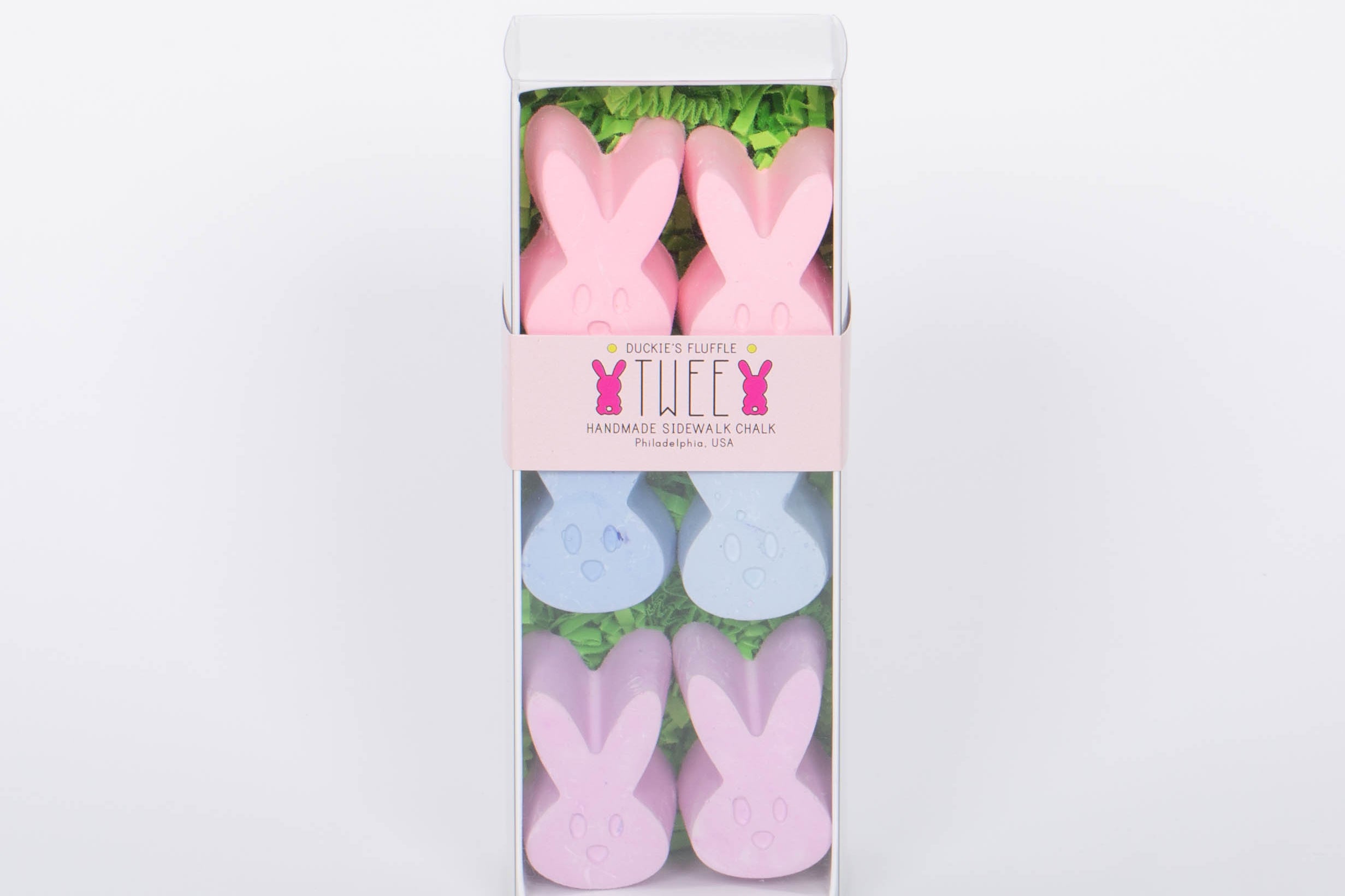 Box of TWEE six piece children's bunny shaped pink, blue, and purple chalk. White background.