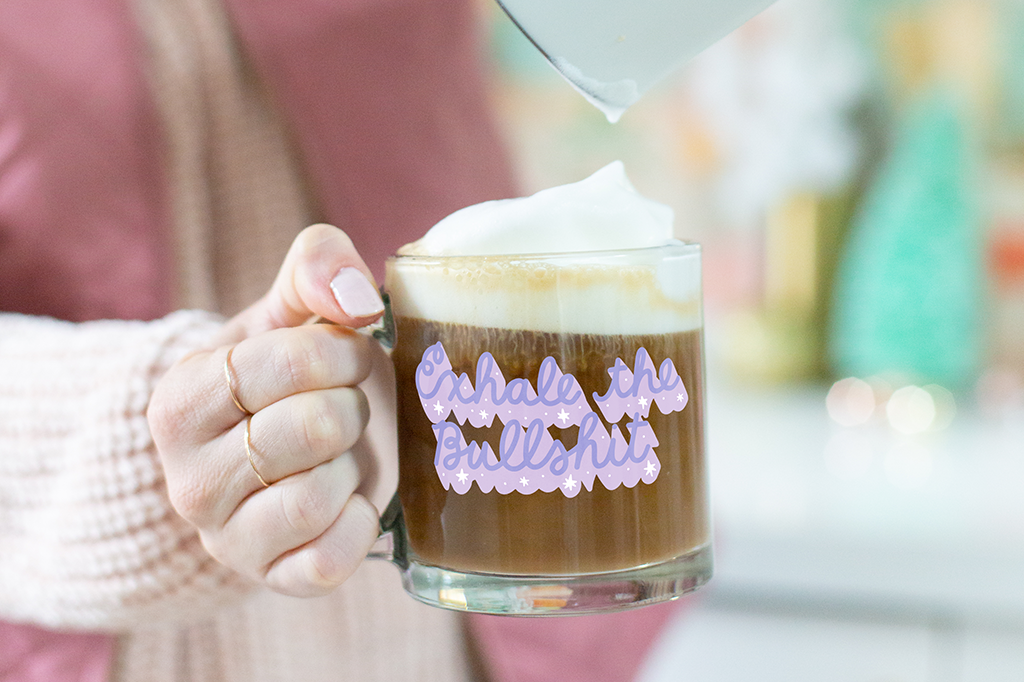 Woman holding "Exhale the Bullshit Mug" with frothy coffee. 
