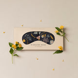 Migraine Mask by Slow North. Strap free cotton weighted eye pillow to be used hot or cold to sooth headaches and tired eyes. Navy and floral print. Inside box surrounded by yellow flowers. 