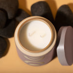 Top view of white candle in blush and tan holder. Lid and coal laying on orange backdrop.