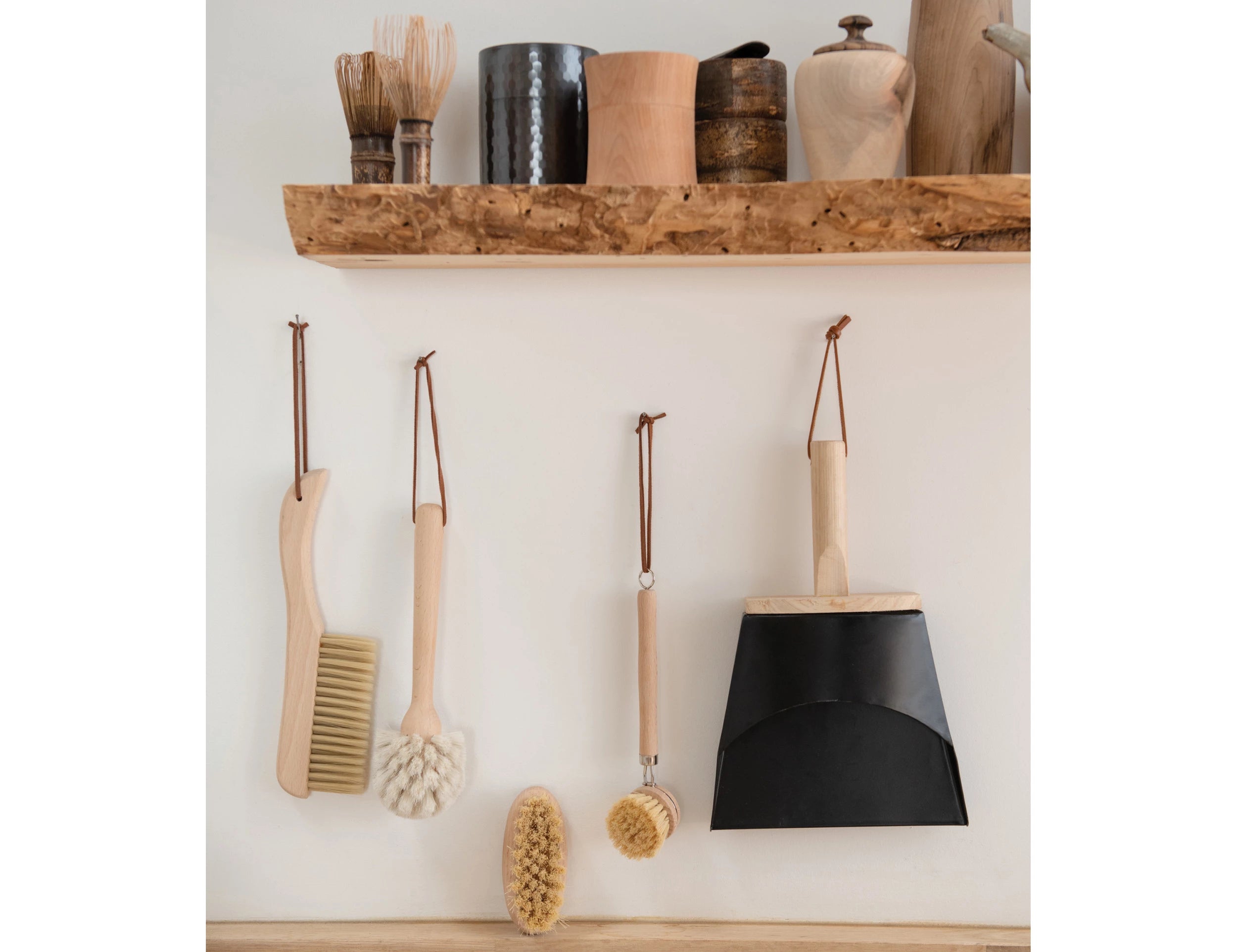 Beech Wood Flat Dish Brush with Leather Strap and silver accents hanging with dustpan and other natural cleaning brushed in neutral washing room.