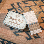 Desert Hills Motel Incense and vintage inspired motel matchbook by Good & Well Supply Co in tan and brown design resting on Southwestern patterned rug. 