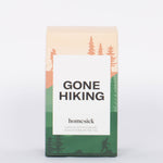 Gone Hiking candle box with pink and green hiking and forest illustration and white label with bold "GONE HIKING" label. 